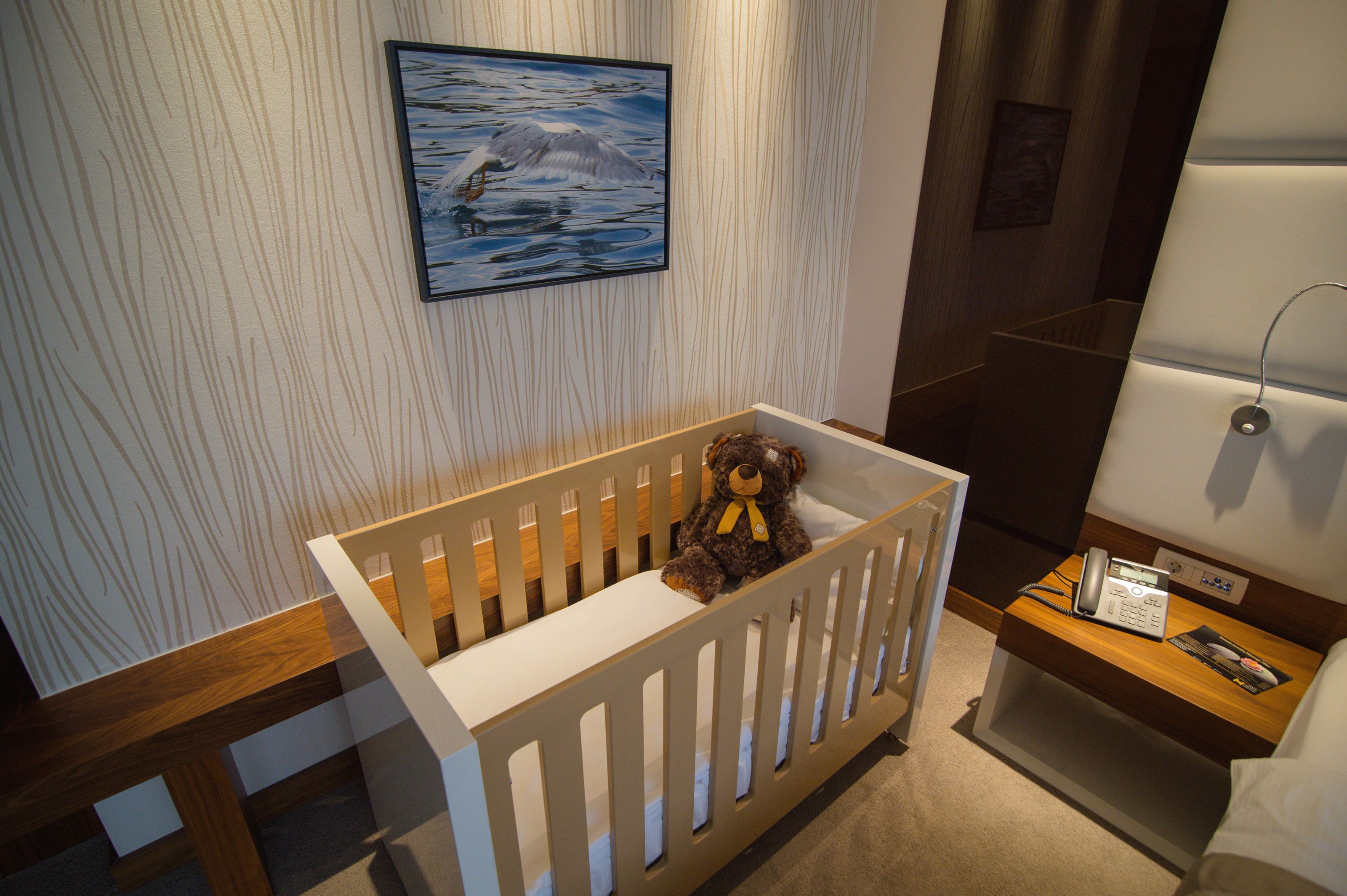 A crib with a teddy bear, a bedside table with a phone, and a framed picture on the wall.