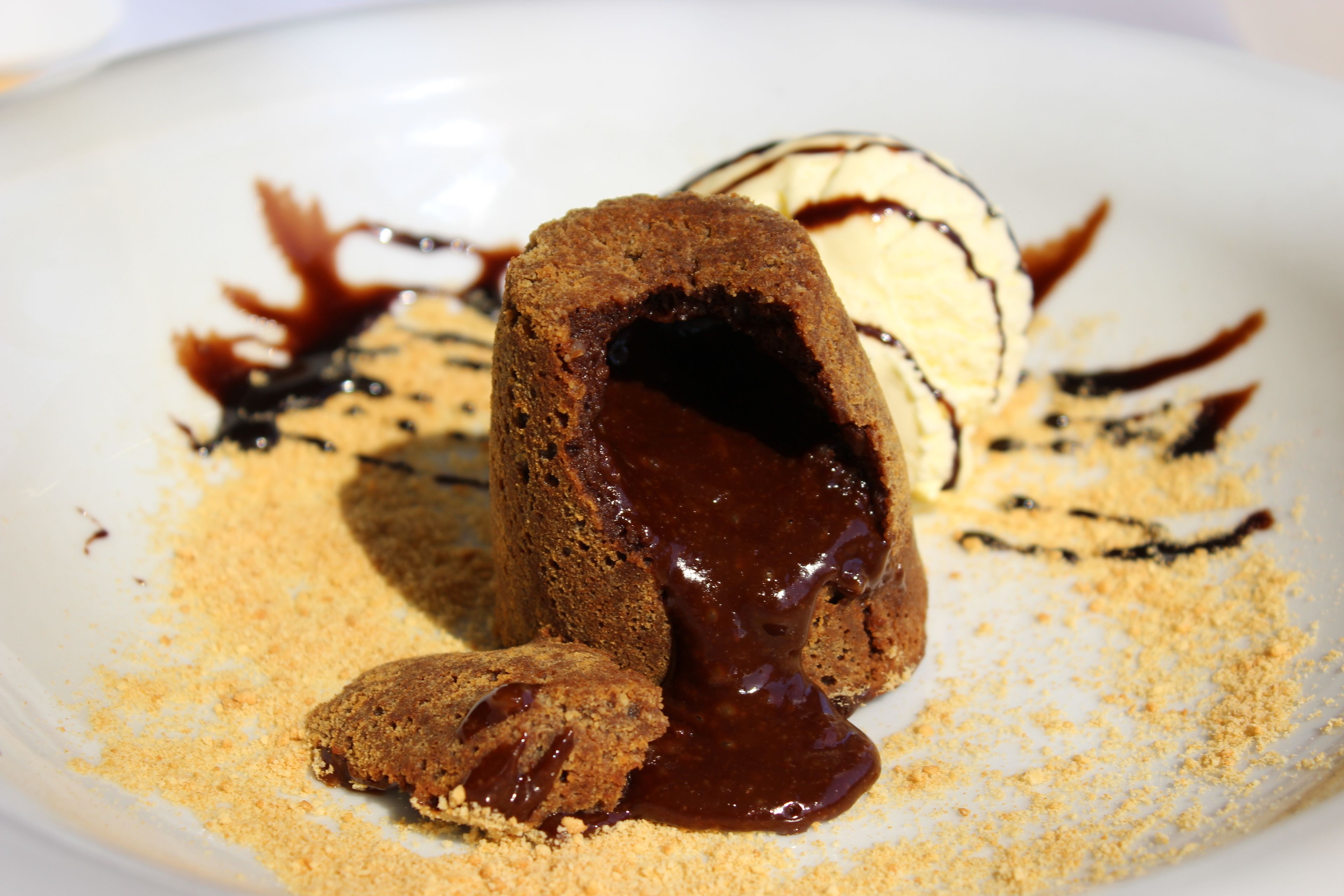 Un postre con centro fundido, rodeado de salsa y migas de chocolate.
