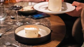 A dining table with a dessert plate, a glass of a light-colored beverage, and a smartphone on the table.