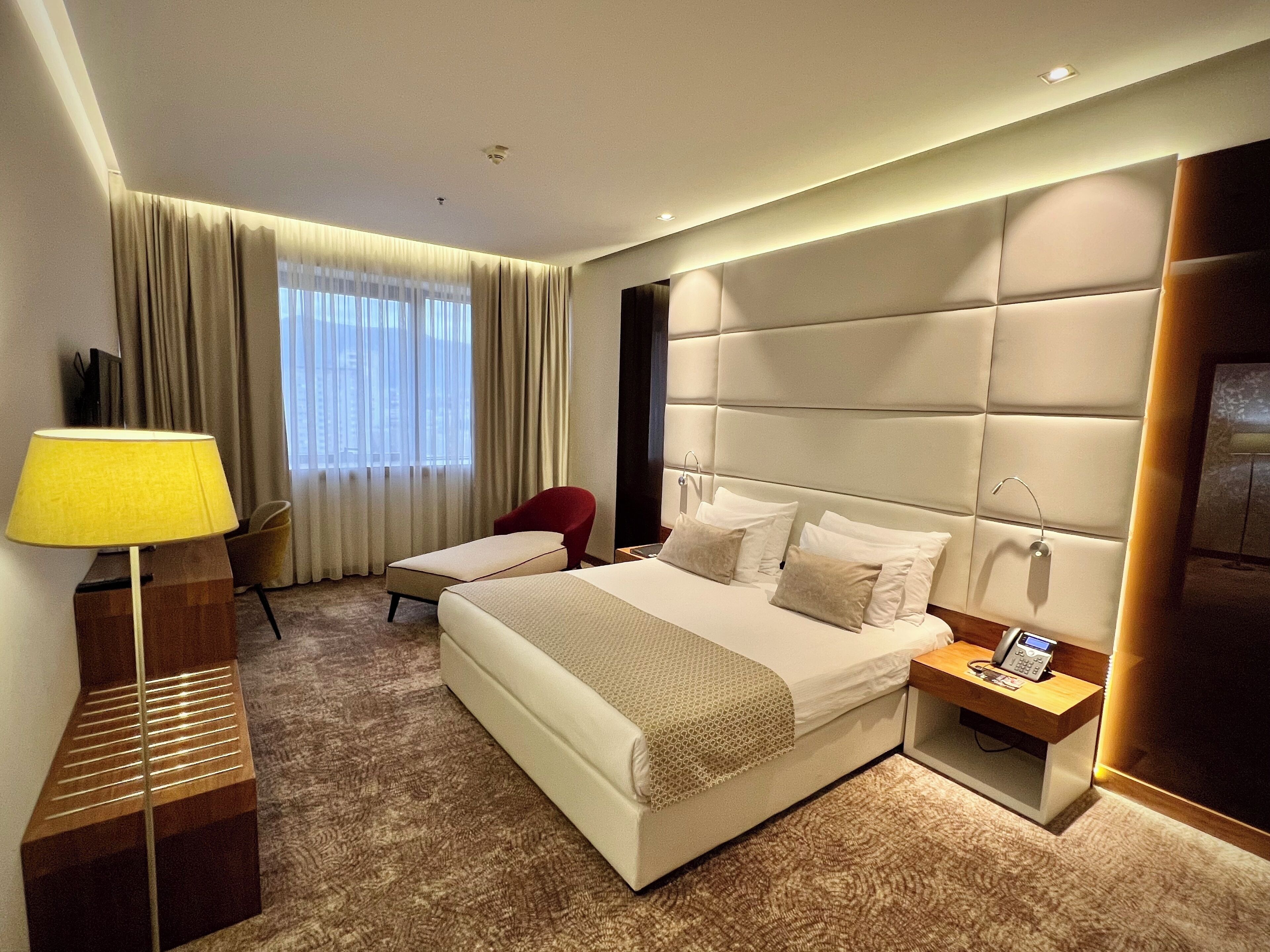 A hotel room with a large bed, bedside tables, a desk, a chair, and a lamp.