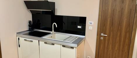 A compact kitchen with a black stove, white cabinets, a stainless steel sink, and a wooden door.