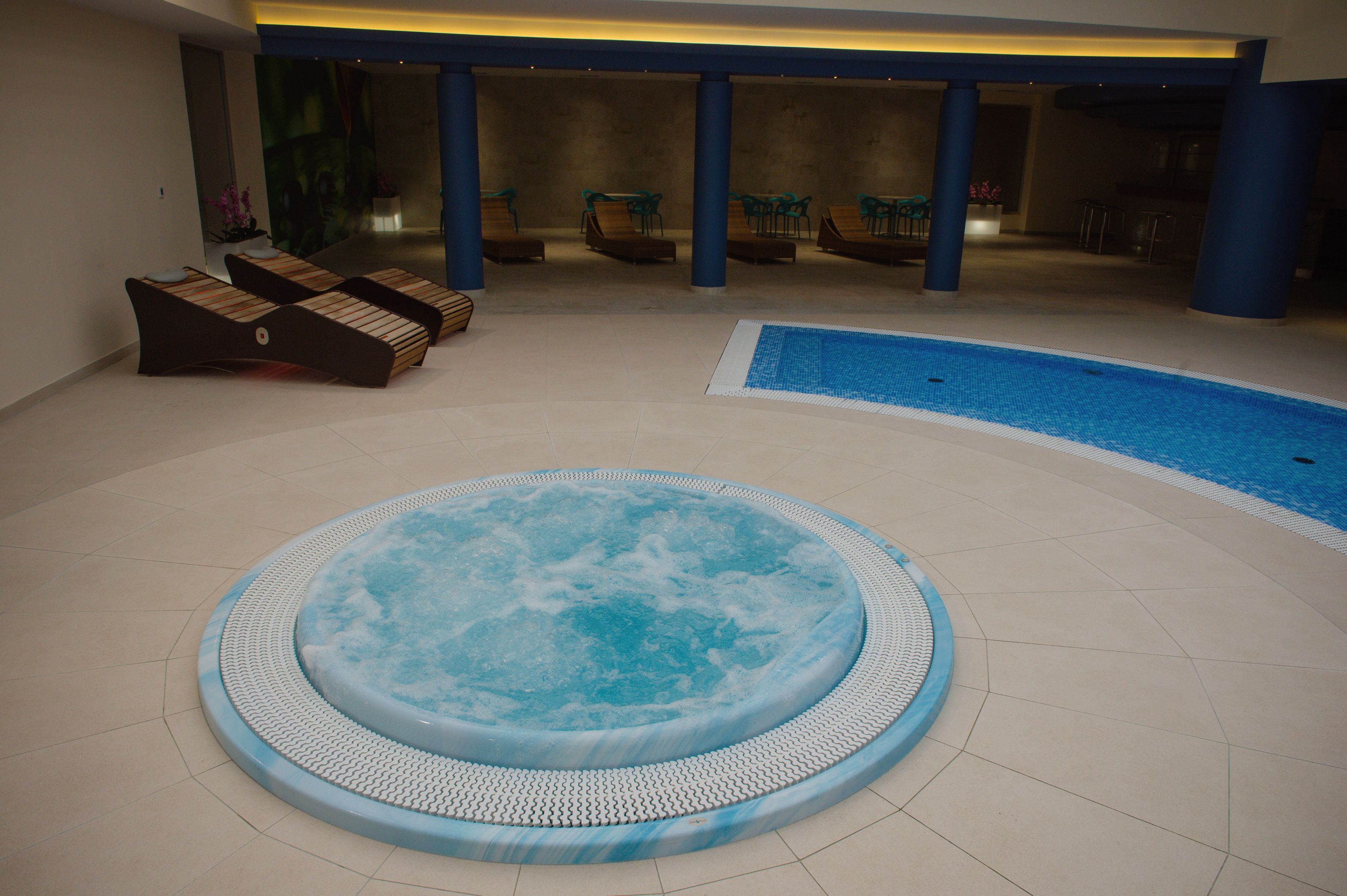 A hot tub and a pool in a spa area with lounge chairs and a bar.