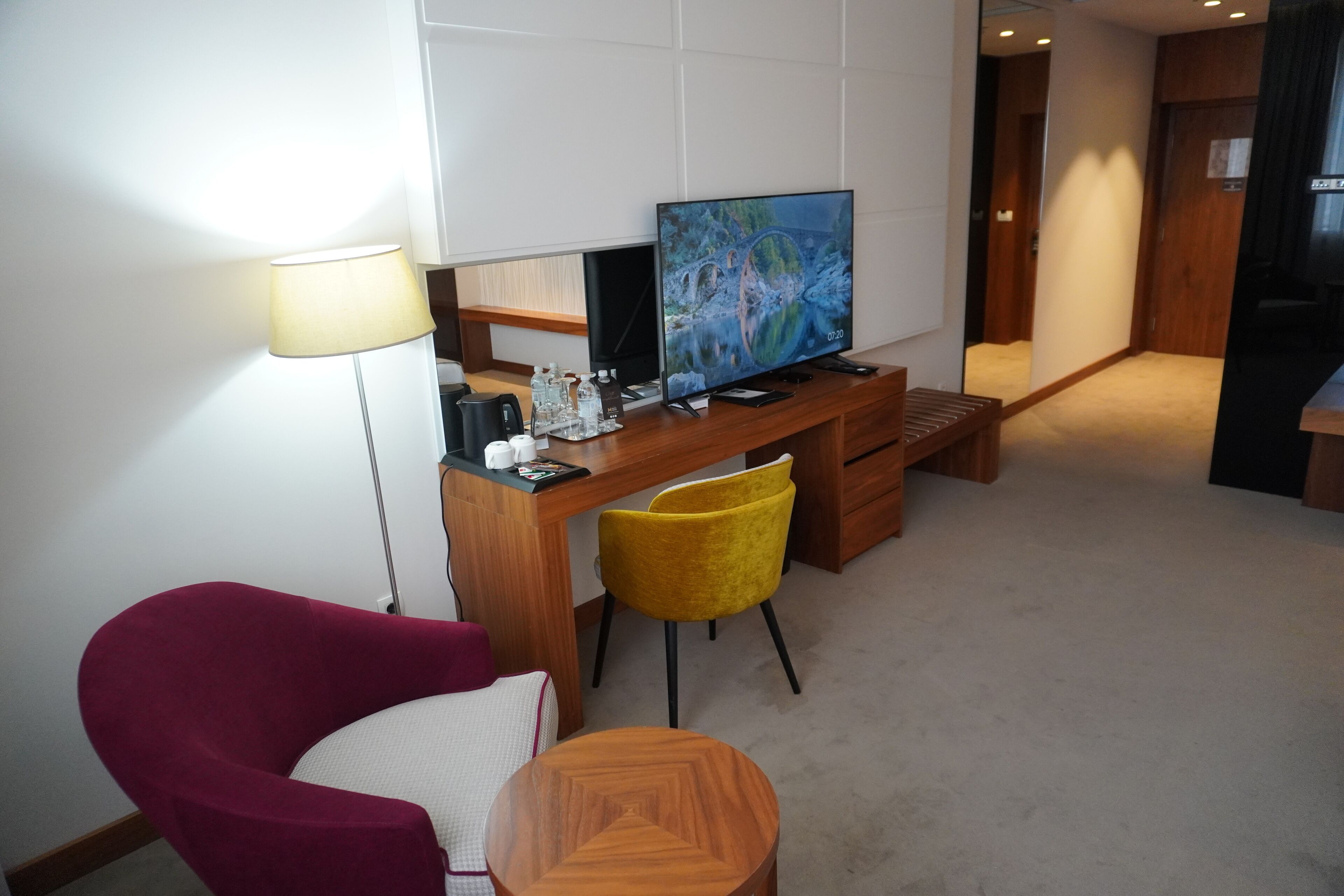 Habitació d'hotel moderna amb escriptori de fusta, televisió de pantalla plana, butaca vermella, cadira groga i petita taula auxiliar de fusta.