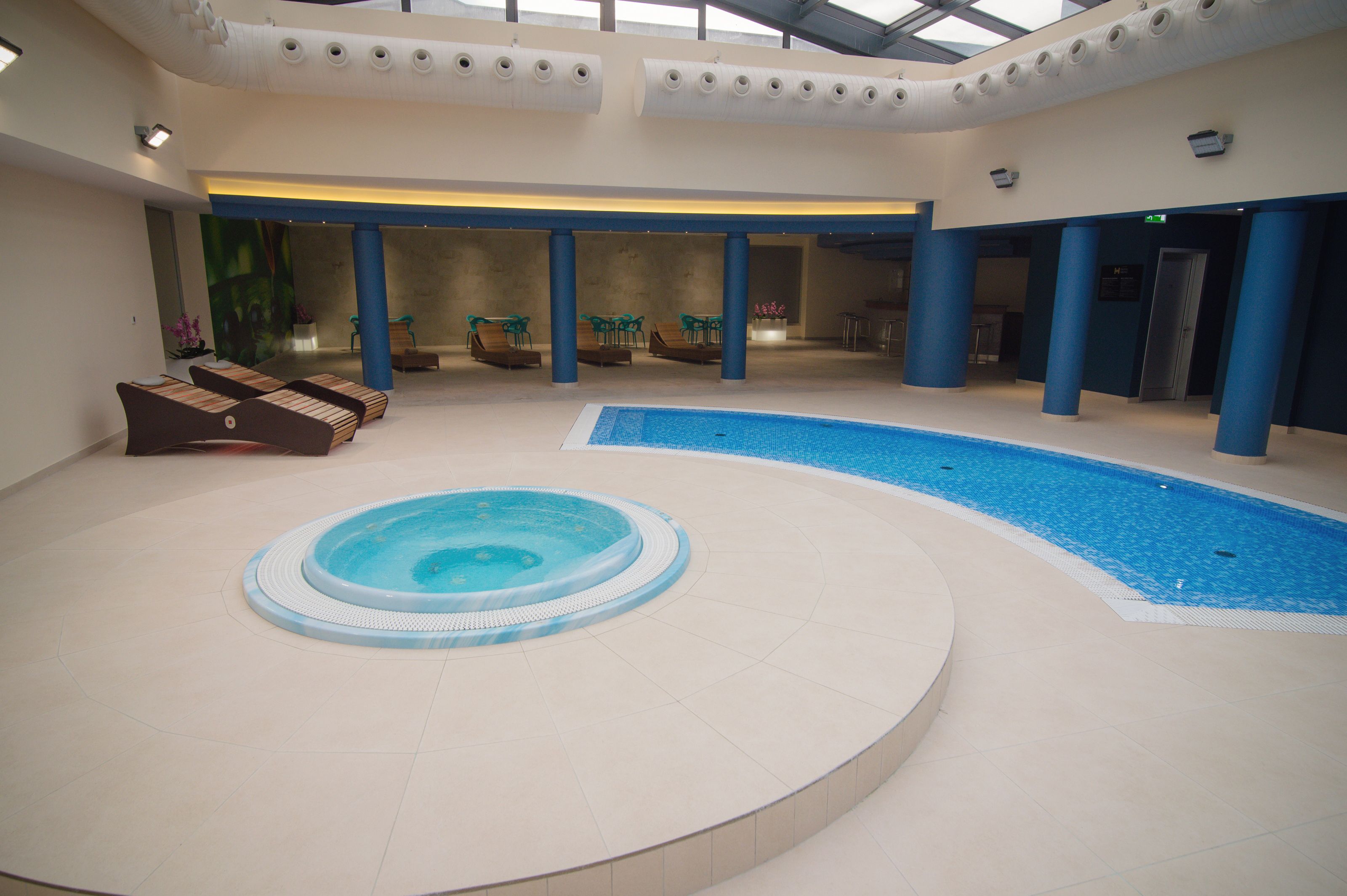 Une piscine intérieure avec un jacuzzi, des chaises longues et un espace salon abrité.