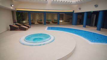 Une piscine intérieure avec un jacuzzi, des chaises longues et un espace salon abrité.