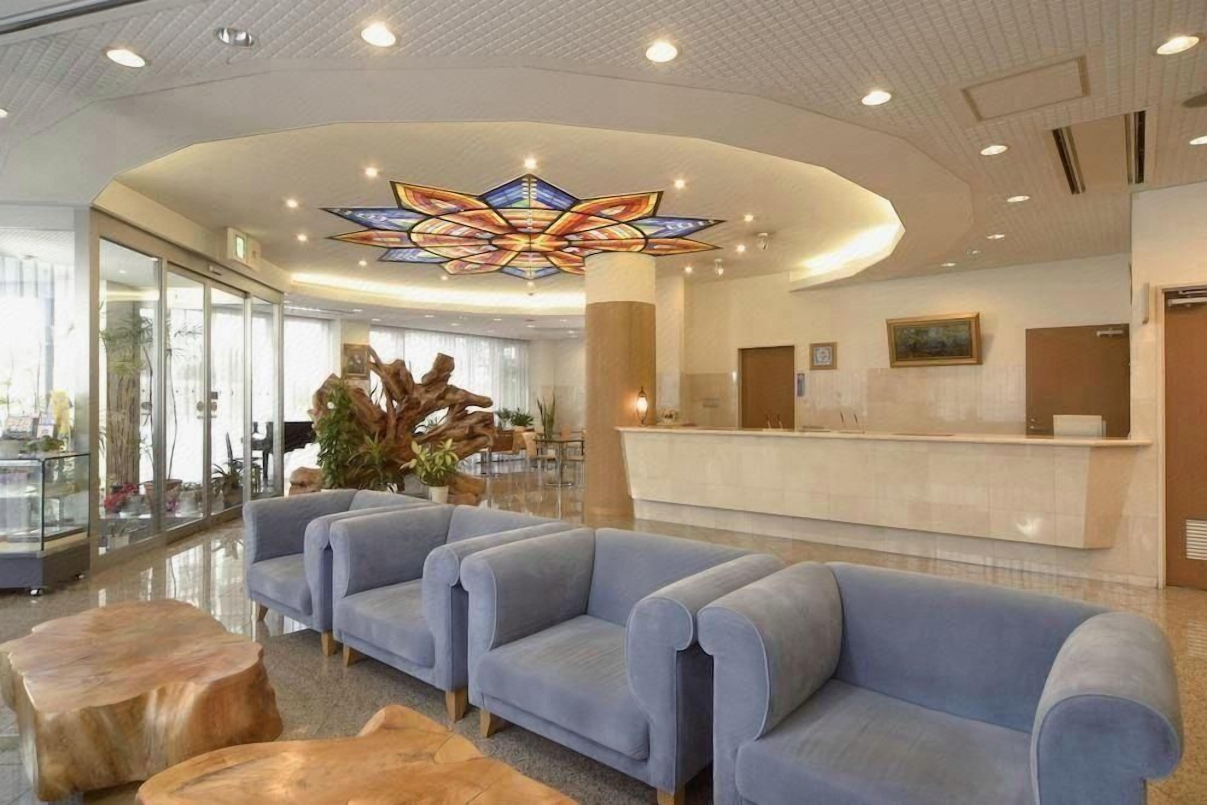 A hotel lobby with a reception desk, blue sofas, and a large stained glass ceiling.