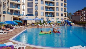 A swimming pool area with lounge chairs and umbrellas, surrounded by a multi-story building with balconies. - Rainbow 1 Holiday Complex (Sunny Beach)