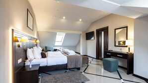 Ein modernes Hotelzimmer mit Bett, Nachttischen, Schreibtisch, Stuhl, Fernseher und einem großen Fenster.