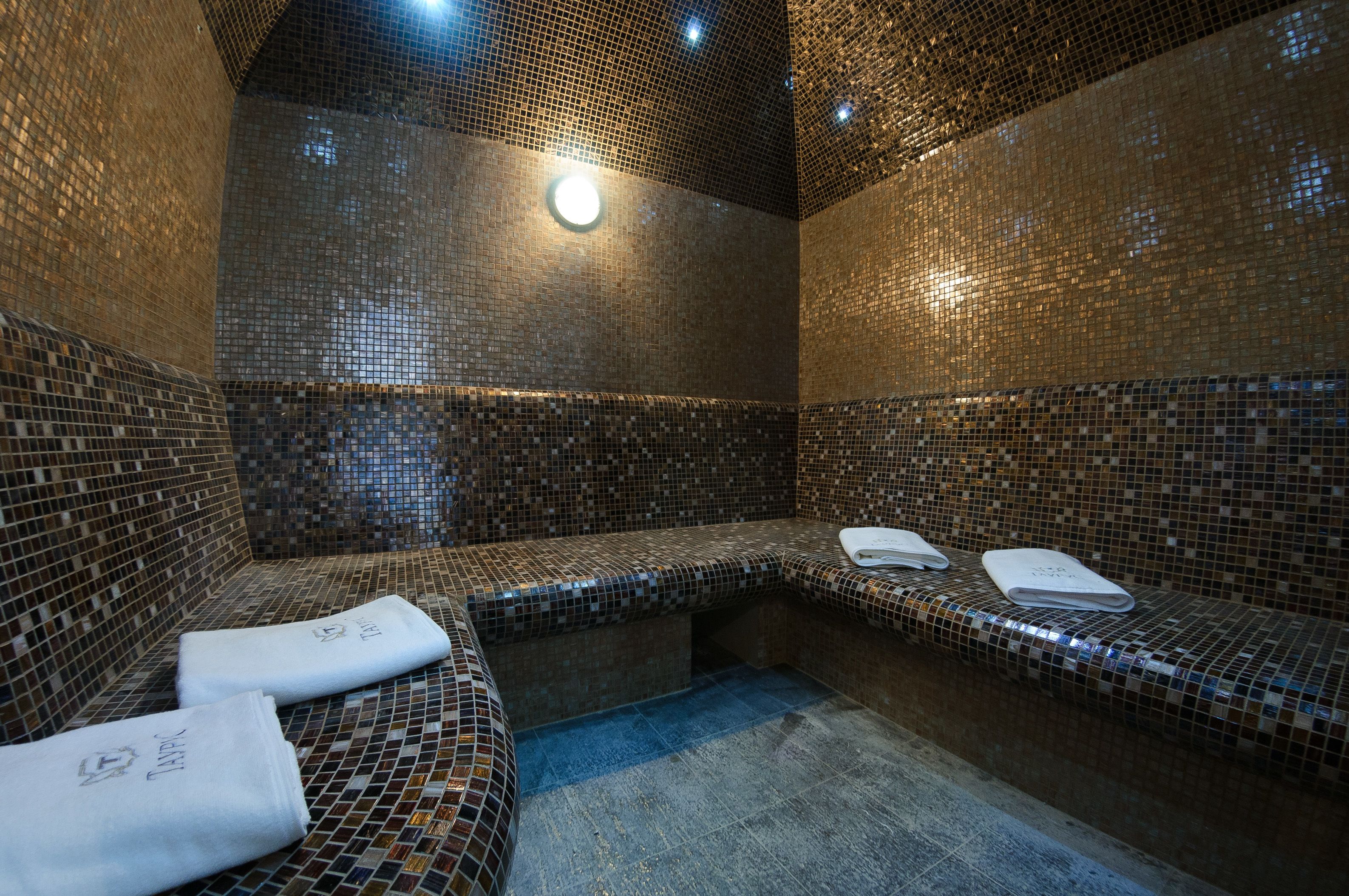 A spa room with mosaic tile walls and benches, towels, and a light fixture.