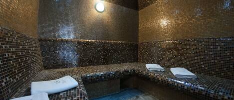 A spa room with mosaic tile walls and benches, towels, and a light fixture.