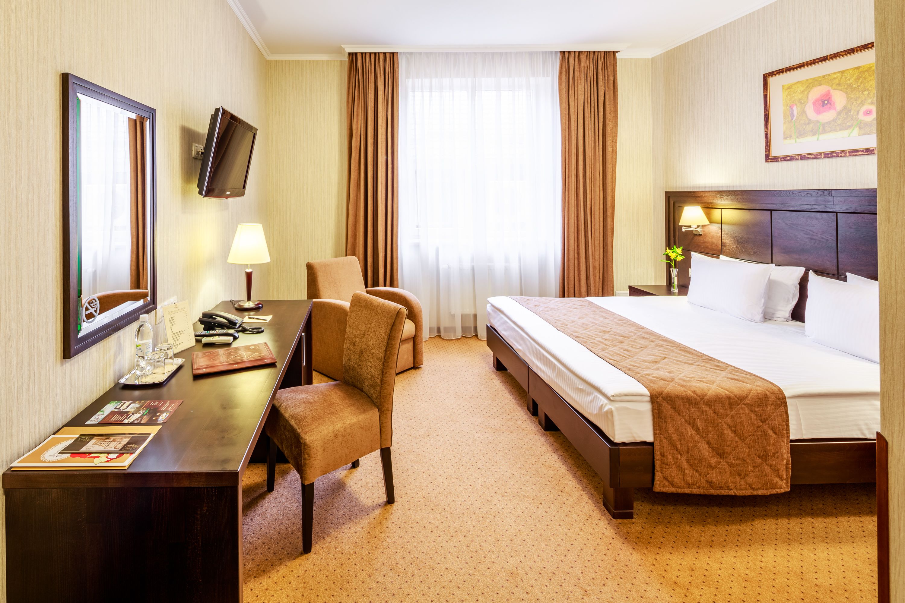 Ein Hotelzimmer mit einem großen Bett, einem Schreibtisch mit Stuhl, einem Fernseher und einem Fenster mit Vorhängen.