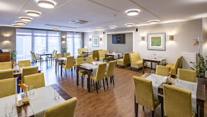 Ein geräumiges Restaurant mit mehreren Tischen und Stühlen, großen Fenstern und modernen Leuchten.