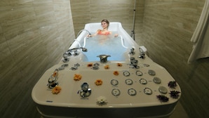 Eine Badewanne mit mehreren Armaturen und eine darin sitzende Person.