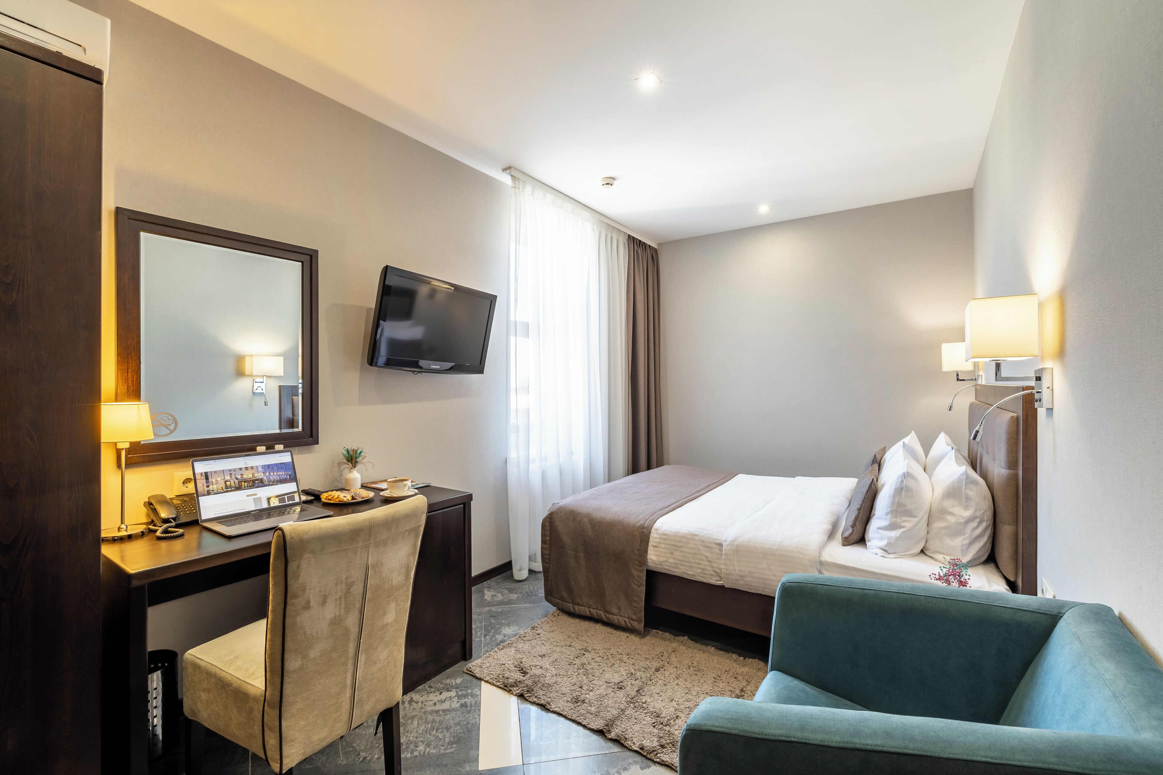 Habitación de hotel con cama, escritorio con una computadora portátil, silla, televisor y sofá.
