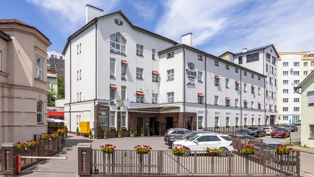 A hotel with a white facade, multiple windows, and a gated entrance with flower boxes. - Taurus Hotel & SPA (Lviv)