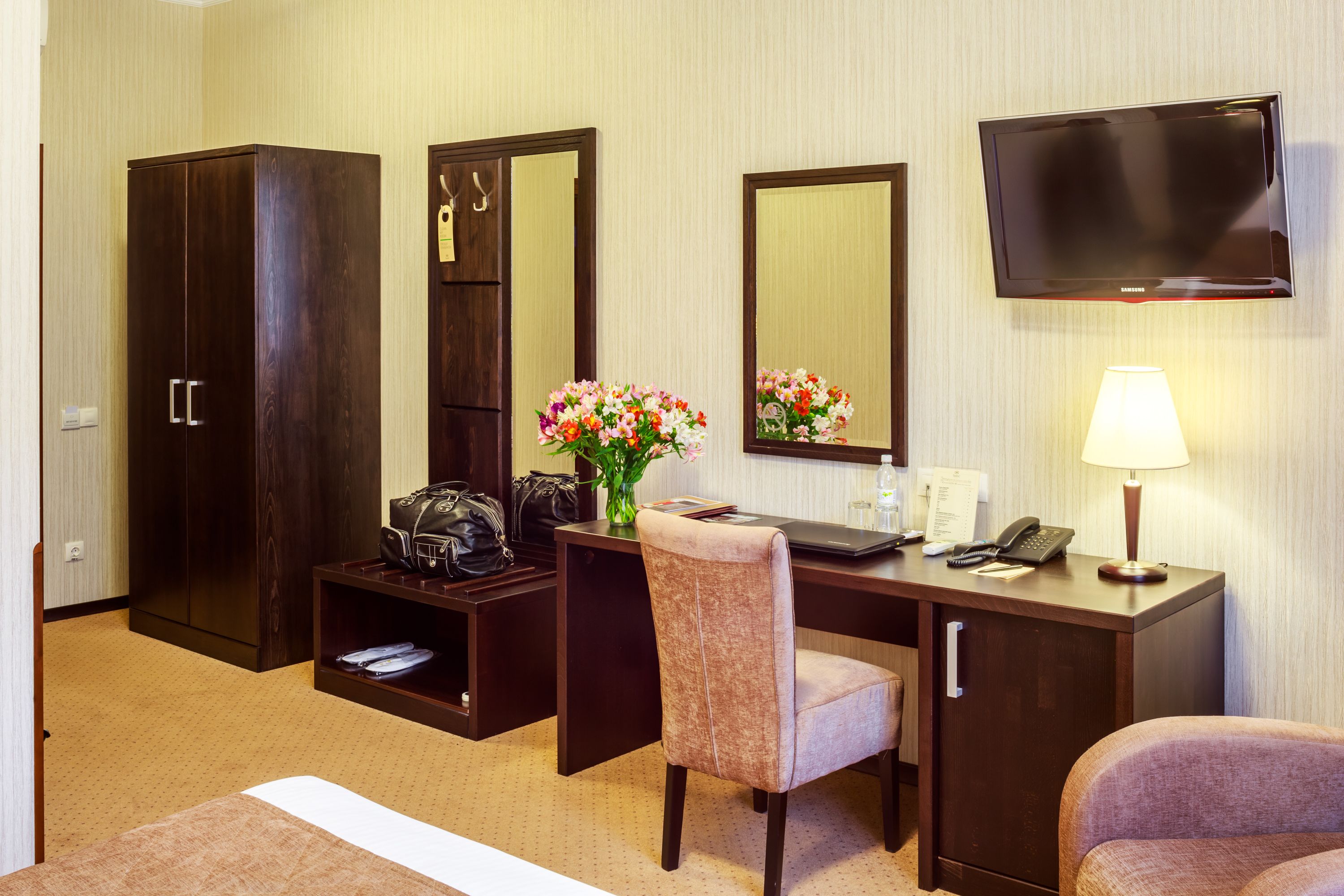 Une chambre d’hôtel équipée d’un bureau, d’une chaise, d’une armoire, d’un miroir, d’une télévision et d’une lampe.
