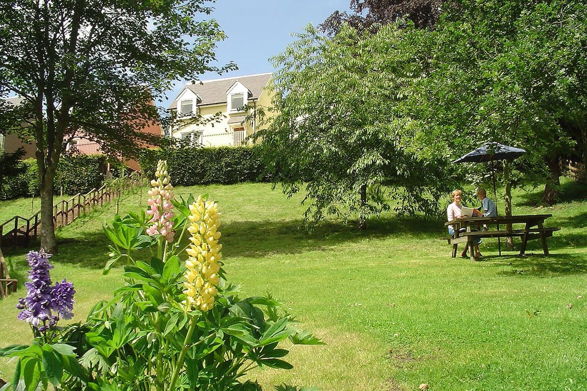 A well-maintained garden with a picnic table and umbrella, surrounded by lush greenery and flowering plants.