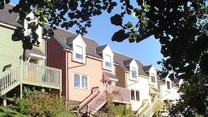 Une rangée de maisons de ville avec des porches à l’avant et une colline couverte d’herbe.
