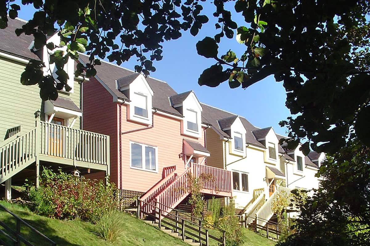 A row of townhouses with a shared staircase, a grassy front yard, and a clear blue sky.