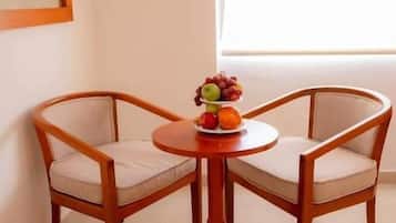 A corner room with two wooden chairs and a small round table with a fruit bowl.