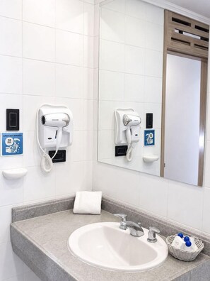 A bathroom with a sink, two hair dryers mounted on the wall, a towel, and a sign indicating a 20-second handwashing requirement.