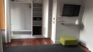 Een kamer met een kledingkast, een aan de muur bevestigde televisie en een klein, groen voetenbankje.