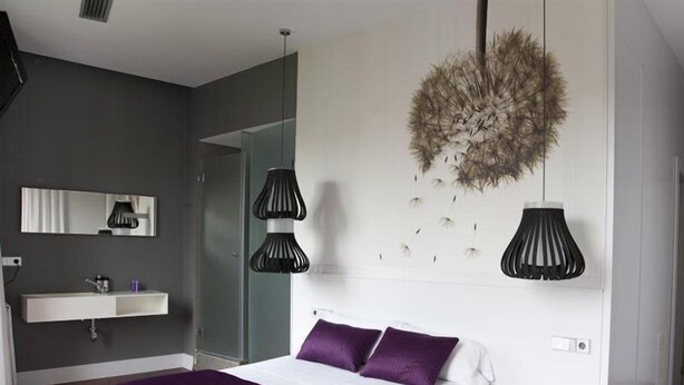 Een moderne slaapkamer met een groot bed, een nachtkastje, een witte nachtkast, een spiegel aan de muur en een hanglamp.