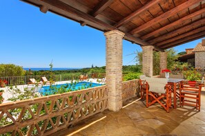 Une terrasse couverte avec une piscine, des meubles en bois et des piliers en pierre.