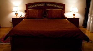 Una cama grande con cabecera de madera, dos mesitas de noche con lámparas y una alfombra roja en el suelo.