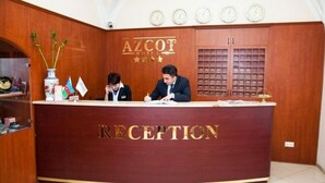 A reception desk at AZCOT Hotel with two staff members, a clock, and a filing cabinet. - Azcot (Baku)