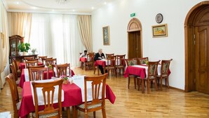 A dining area with tables covered in red tablecloths, wooden chairs, and a chandelier. - Azcot (Baku)