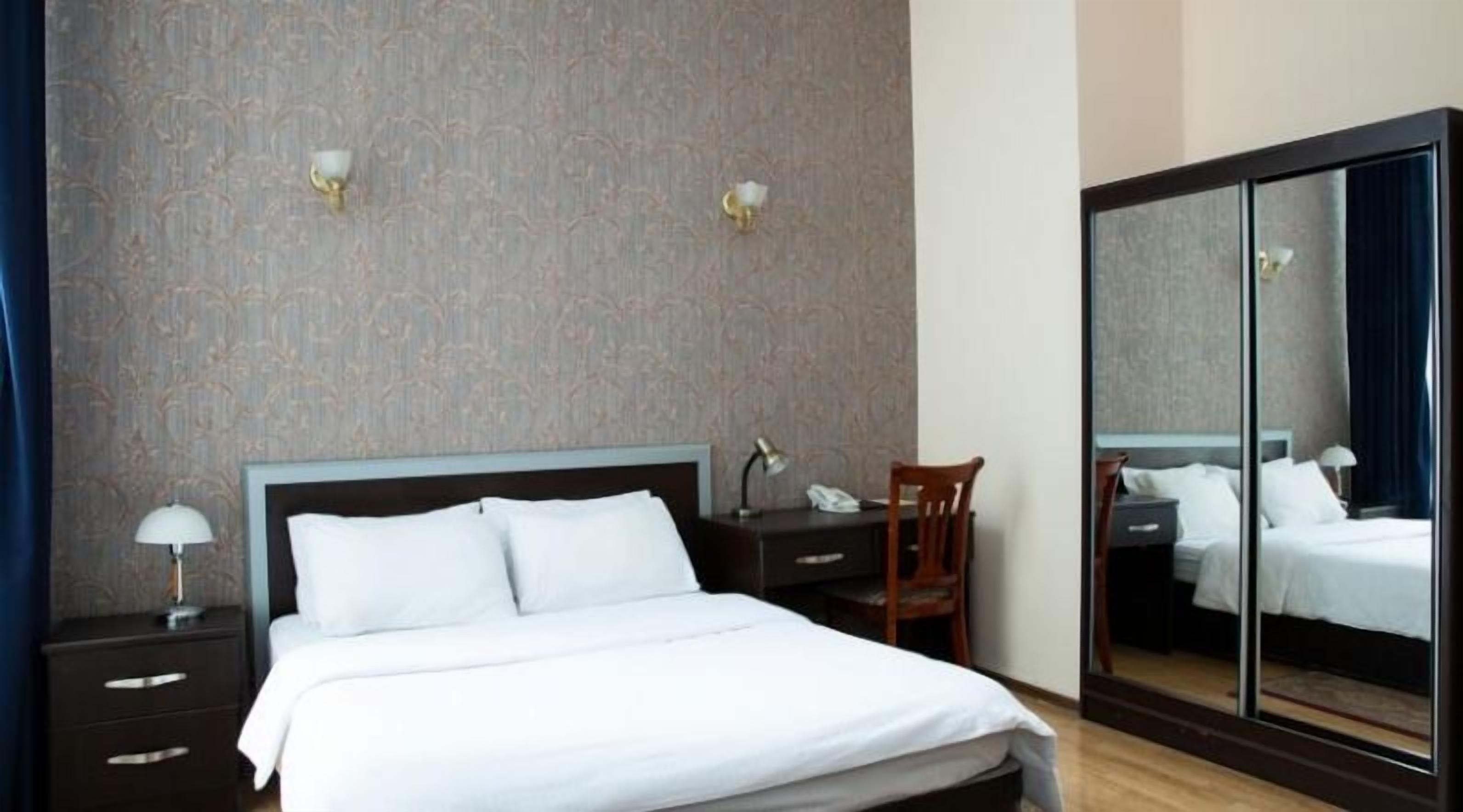 Une chambre d’hôtel comprenant un lit, un bureau avec une chaise, un miroir et une table de chevet avec une lampe.