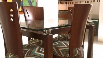 Comedor con una mesa de vidrio rodeada de sillas de madera con cojines estampados.