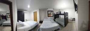 A hotel room with three single beds, a wardrobe, a television, and a mirror.
