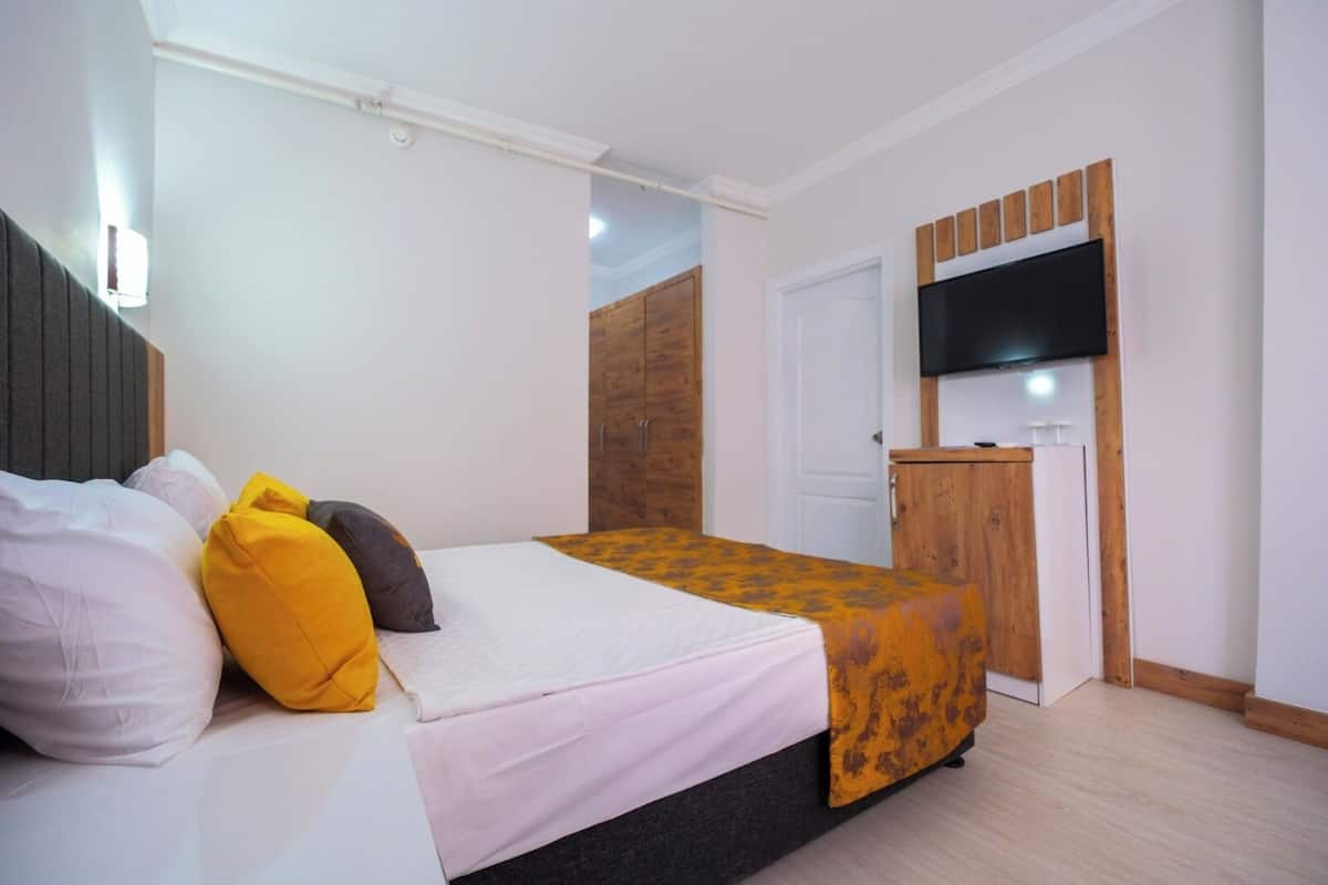 A bedroom with a bed, a TV mounted on the wall, and a wooden wardrobe.