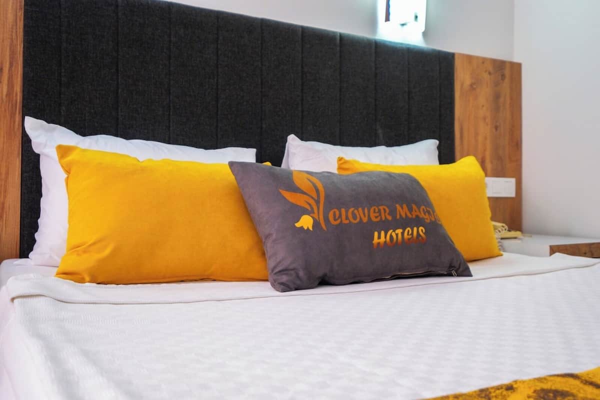 A bed with white bedding and two pillows, one yellow and one with 'Clover Magic Hotels' text.