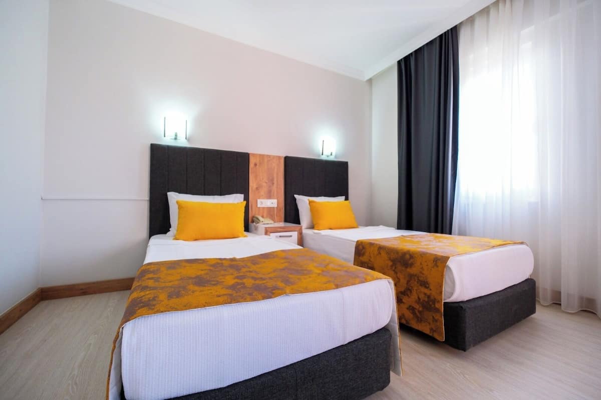 A hotel room with two beds, each with a headboard, a nightstand, and a lamp.