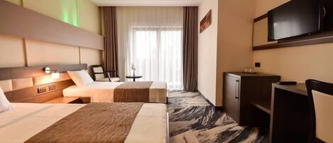 A hotel room with two beds, a desk, a television, and a window with curtains.