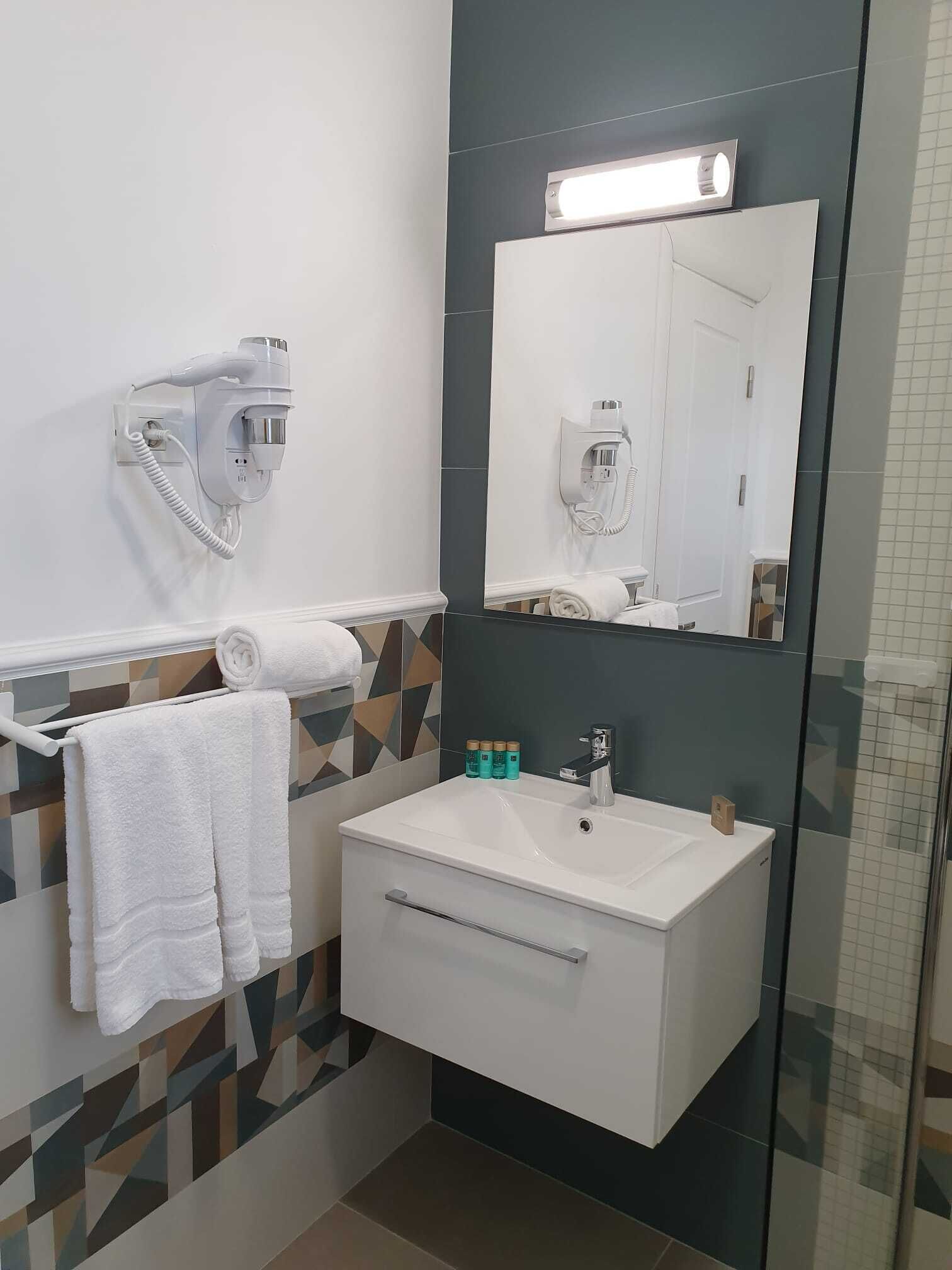 Une salle de bain moderne avec un lavabo blanc, un miroir et un sèche-cheveux fixé au mur.