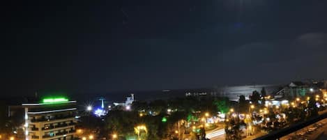 A nighttime cityscape with illuminated buildings, a busy street, and a distant bridge.