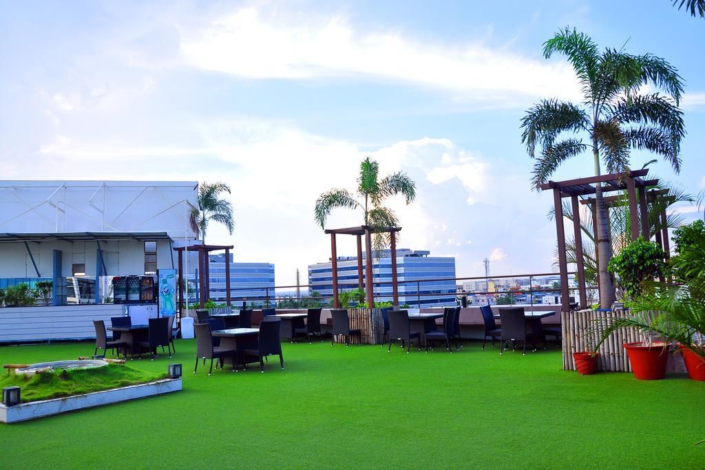 An outdoor seating area with tables and chairs, surrounded by greenery and palm trees.