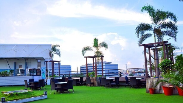 An outdoor seating area with tables and chairs, surrounded by greenery and palm trees. - Gokulam Park Sabari OMR Hotel (Tirupporur)