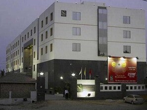 A multi-story building with a flat facade, a large illuminated sign on the right, and a person walking in front. - Gokulam Park Sabari OMR Hotel (Tirupporur)