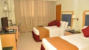 A hotel room with two beds, a desk with a chair, a mirror, and a window with curtains. - Gokulam Park Sabari OMR Hotel (Tirupporur)