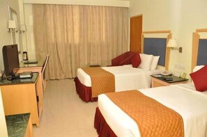 A hotel room with two beds, a desk with a chair, a mirror, and a window with curtains. - Gokulam Park Sabari OMR Hotel (Tirupporur)