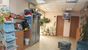 Zona de recepción con mostrador, refrigerador de Pepsi, plantas en macetas, área de descanso y televisor.