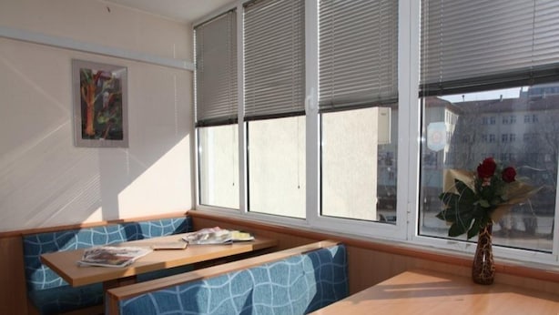 Una habitación con ventana, un banco, una mesa y un jarrón con flores.