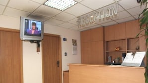 Un área de recepción con un televisor montado en la pared, armarios de madera y un mostrador de recepción.