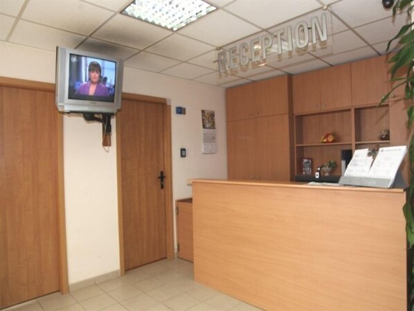 A reception area with a television mounted on the wall, wooden cabinets, and a reception desk.