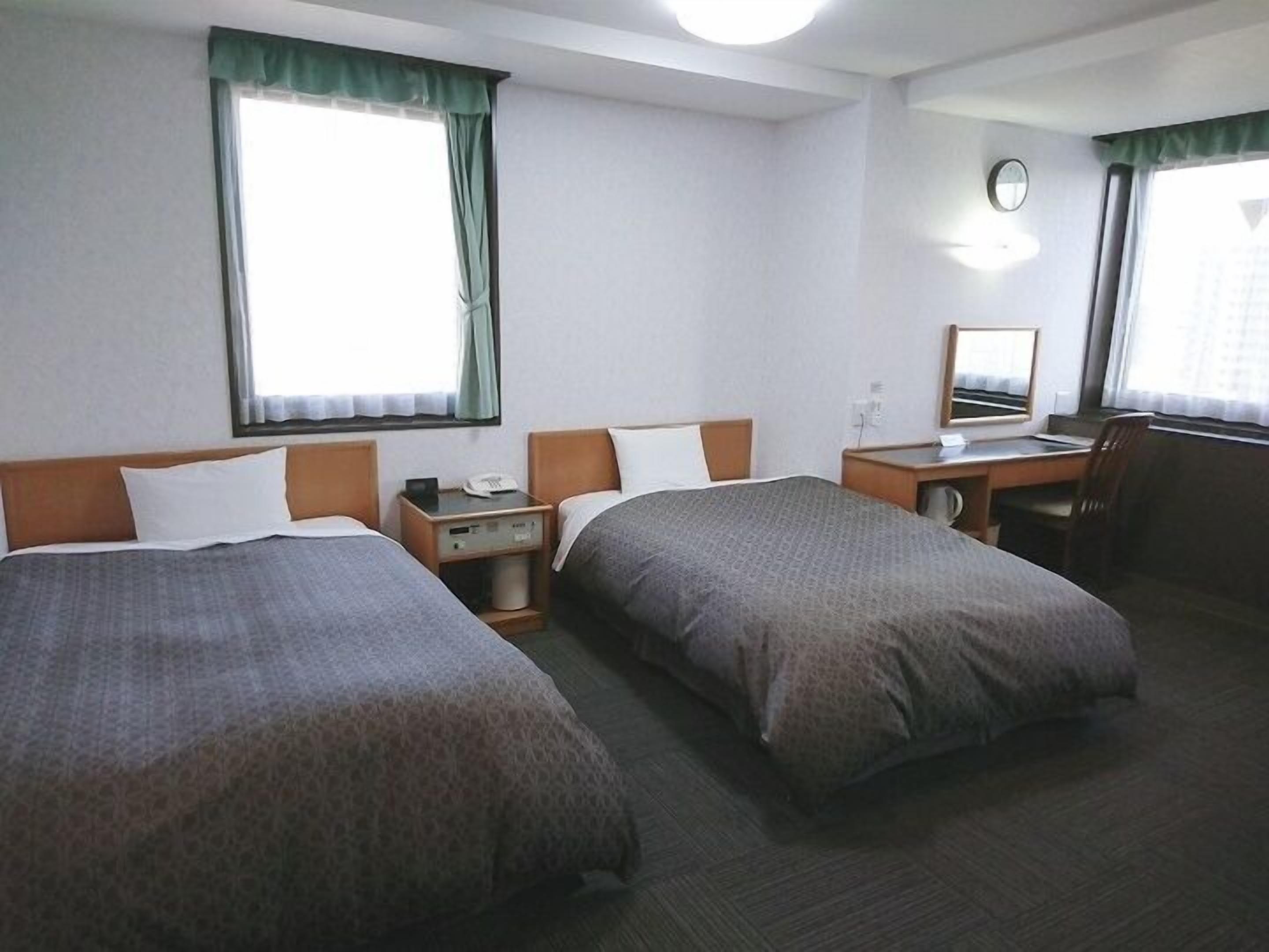 A hotel room with two single beds, a desk with a chair, a small table with a phone, and a mirror.